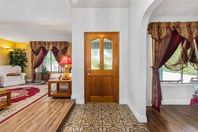 foyer featuring arched walkways, wood finished floors, and baseboards