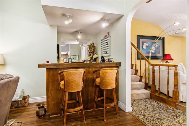 indoor dry bar featuring wood finished floors, baseboards, arched walkways, and stairway