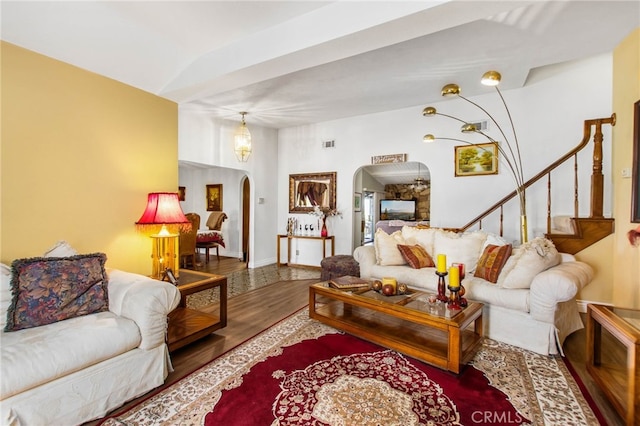 living area with arched walkways, wood finished floors, and stairs