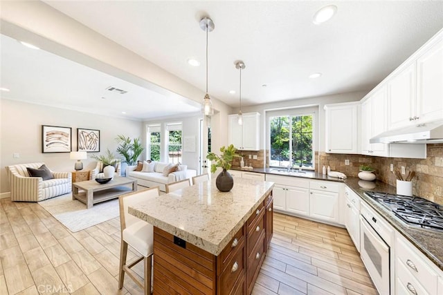 107 Plaza Via Sol, San Clemente, CA 92673 - kitchen featuring stainless steel gas stovetop, open floor plan, under cabinet range hood, decorative backsplash, and light wood-type flooring