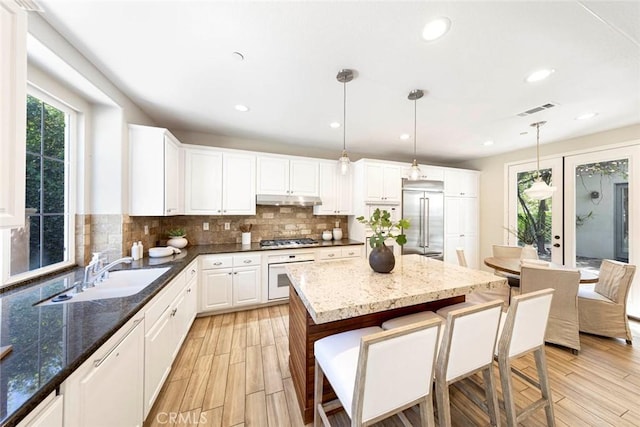 107 Plaza Via Sol, San Clemente, CA 92673 - kitchen with stainless steel appliances, a sink, under cabinet range hood, a kitchen breakfast bar, and tasteful backsplash