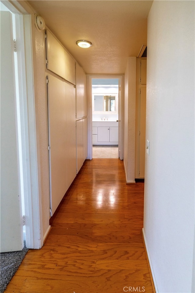 corridor with light wood-style floors, a sink, and baseboards