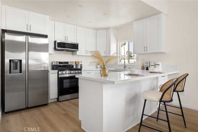 kitchen featuring stainless steel appliances, a sink, a breakfast bar area, white cabinetry, and light countertops