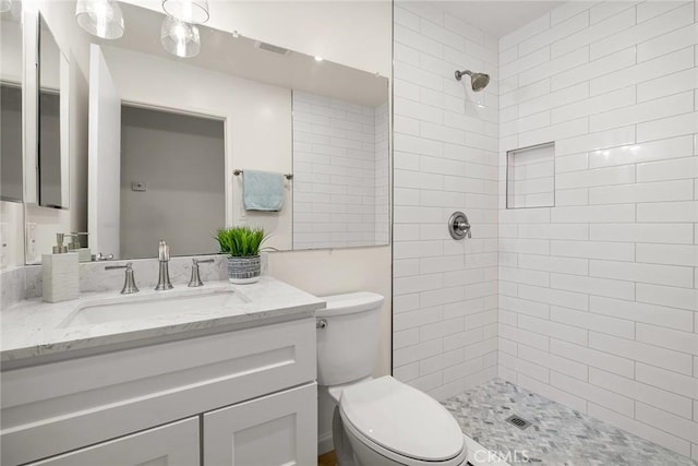 bathroom featuring toilet, tiled shower, and vanity