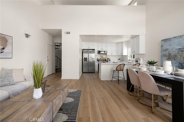 living area featuring a towering ceiling, light wood-style flooring, and stairway