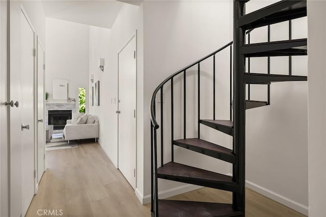 stairway featuring wood finished floors, a fireplace, baseboards, and a high ceiling