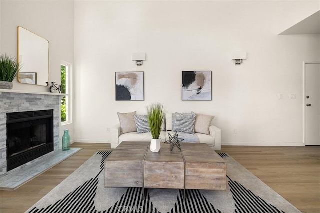 living area featuring wood finished floors, baseboards, and a stone fireplace