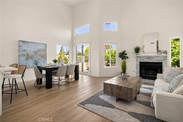 living area with light wood-style flooring, a high ceiling, a fireplace with flush hearth, and baseboards