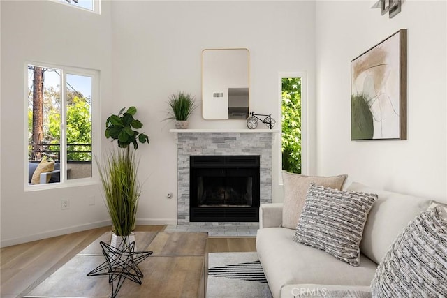 living area with wood finished floors, a towering ceiling, a fireplace with flush hearth, and baseboards