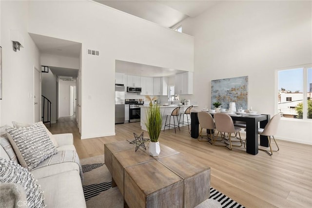 living area featuring a towering ceiling, light wood finished floors, baseboards, and stairs