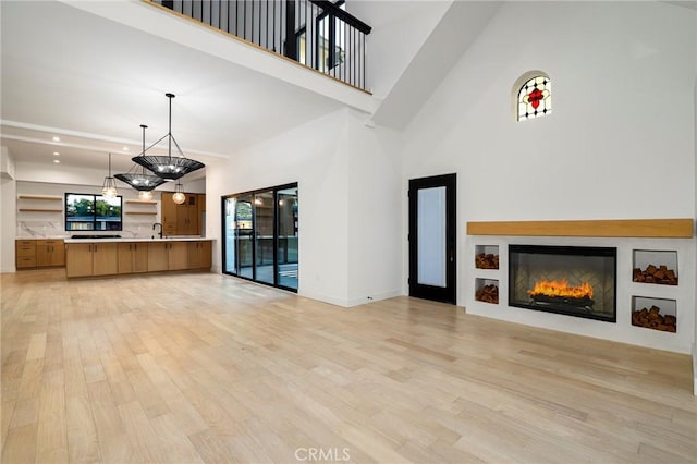 5633 E Deborah St, Long Beach, CA 90815 - unfurnished living room with light wood-type flooring, a glass covered fireplace, a towering ceiling, recessed lighting, and baseboards