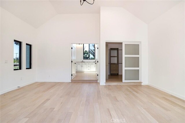 5633 E Deborah St, Long Beach, CA 90815 - unfurnished living room featuring high vaulted ceiling, light wood finished floors, healthy amount of natural light, a chandelier, and baseboards