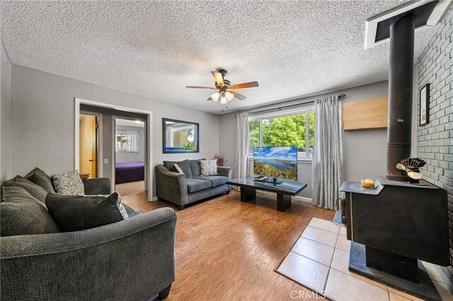 3595 Vista St, Clearlake, CA 95422 - living room featuring a wood stove, ceiling fan, light wood finished floors, and a textured ceiling