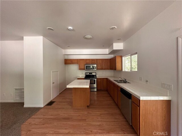 9345 Conifer Dr, Forest Falls, CA 92339 - kitchen featuring appliances with stainless steel finishes, brown cabinetry, a kitchen island, light wood-style flooring, and tile counters