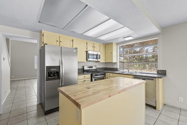 1561 Parkland Way, San Diego, CA 92114 - kitchen with appliances with stainless steel finishes, light tile patterned floors, a center island, butcher block countertops, and cream cabinetry