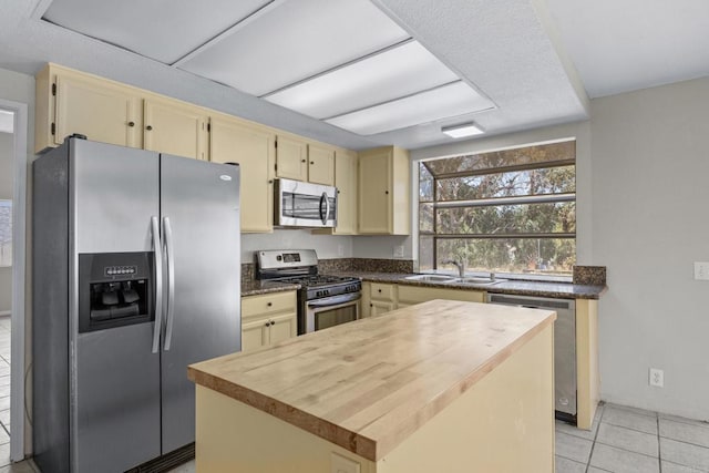 1561 Parkland Way, San Diego, CA 92114 - kitchen featuring appliances with stainless steel finishes, cream cabinetry, light tile patterned flooring, a kitchen island, and butcher block counters
