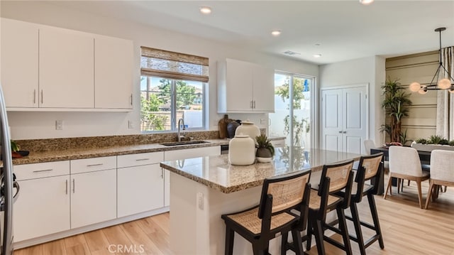30025 Adrift Ln, Menifee, CA 92584 - kitchen featuring a sink, light wood finished floors, white cabinets, decorative light fixtures, and light stone counters