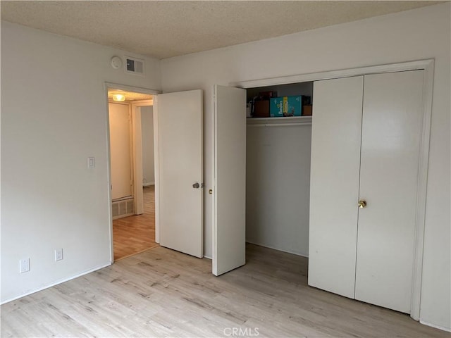 unfurnished bedroom with light wood-type flooring, a closet, and a textured ceiling