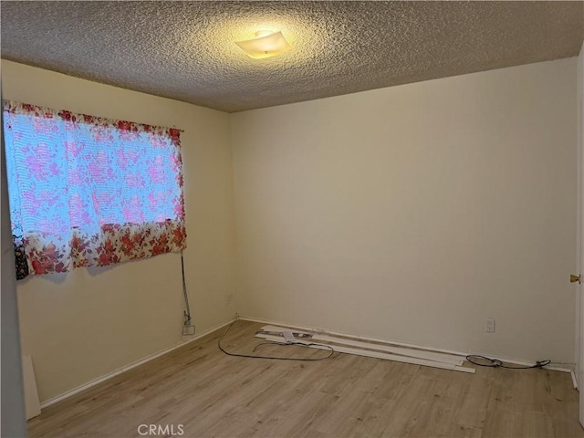 spare room featuring light wood finished floors, a textured ceiling, and baseboards