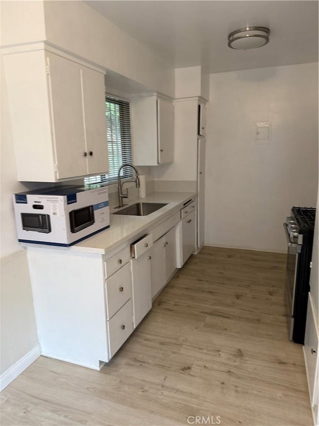 kitchen featuring white appliances, a sink, light countertops, light wood-type flooring, and white cabinets