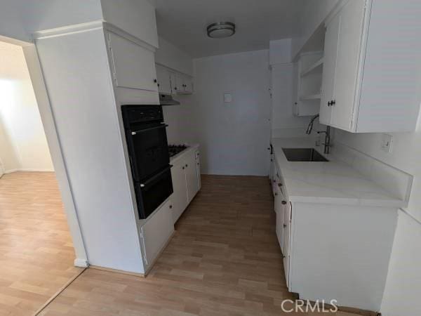 kitchen with a sink, black appliances, a warming drawer, and light wood finished floors