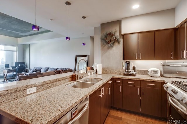 kitchen featuring a sink, stainless steel appliances, open floor plan, a peninsula, and light wood-style flooring