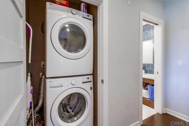 laundry room with stacked washing machine and dryer, baseboards, and wood finished floors