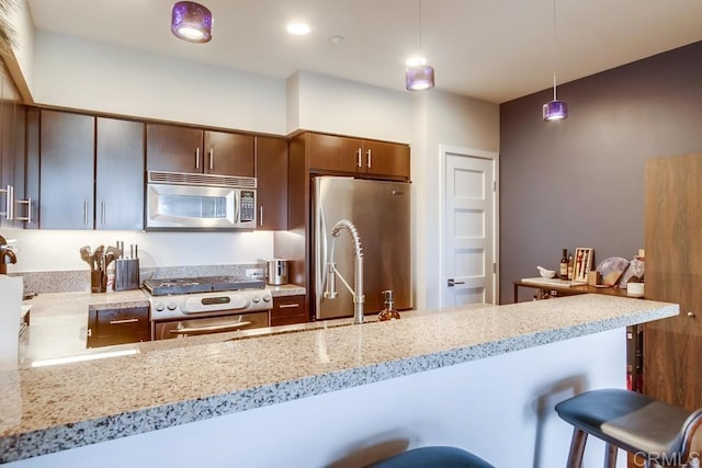 kitchen with appliances with stainless steel finishes, a breakfast bar area, light stone counters, pendant lighting, and a sink