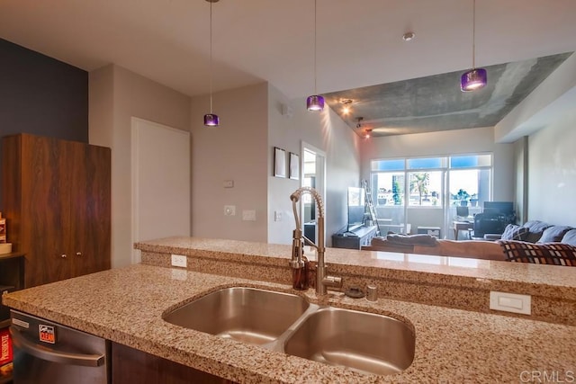 kitchen with a sink, open floor plan, light stone counters, and decorative light fixtures