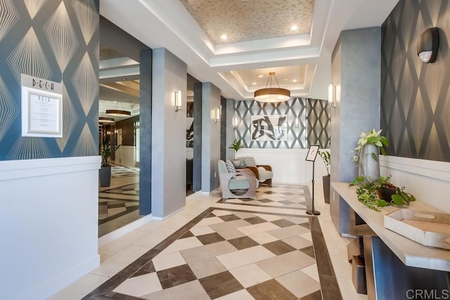 corridor with a raised ceiling, recessed lighting, inlaid floor details, baseboards, and light tile patterned floors