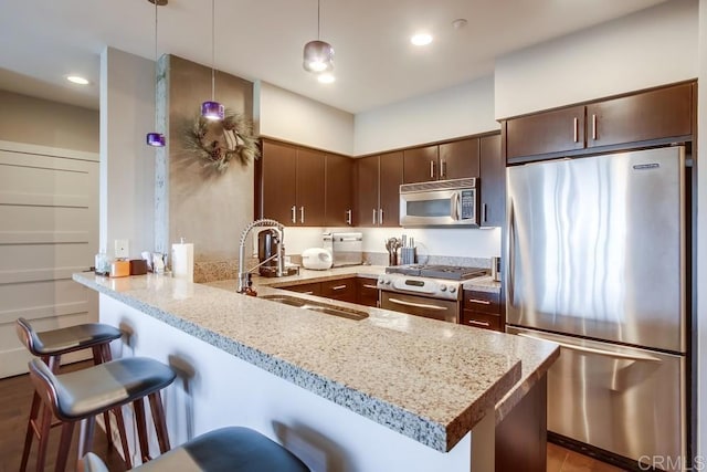 kitchen with stainless steel appliances, a peninsula, a breakfast bar area, dark brown cabinets, and a sink
