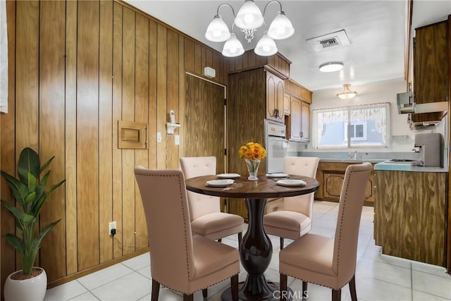 dining space with light tile patterned floors, wooden walls, and a chandelier