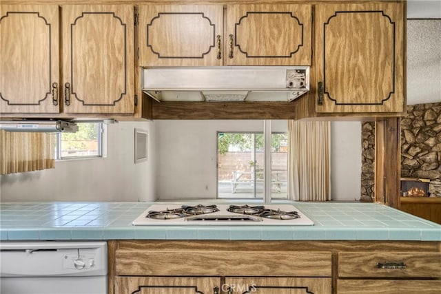 kitchen featuring under cabinet range hood, white appliances, plenty of natural light, and tile counters