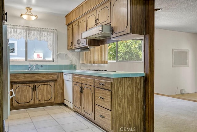 kitchen with under cabinet range hood, brown cabinetry, white dishwasher, a sink, and a textured ceiling