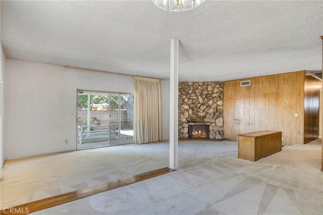 unfurnished living room with a stone fireplace, a textured ceiling, carpet flooring, and wood walls