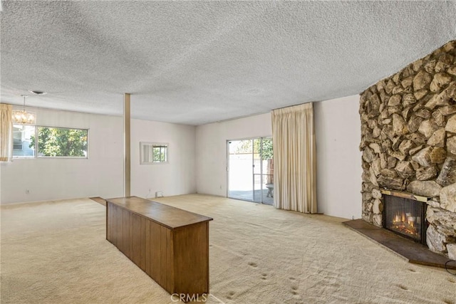 unfurnished living room with carpet floors, a fireplace, plenty of natural light, a chandelier, and a textured ceiling