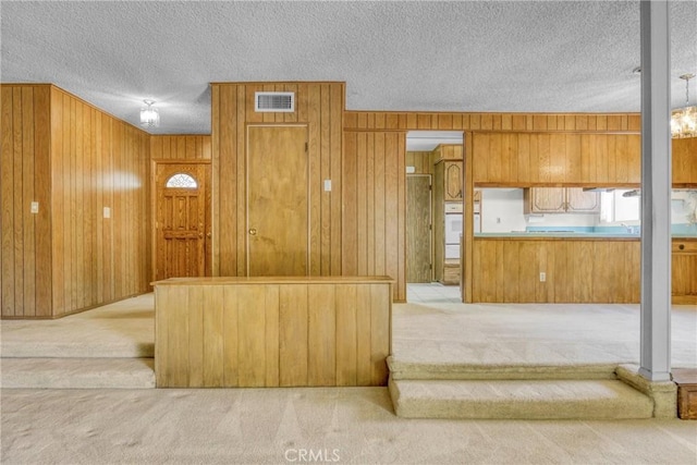 kitchen featuring carpet, wood walls, a textured ceiling, and brown cabinetry