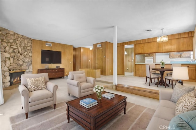 living room featuring light colored carpet, wooden walls, a fireplace, and a chandelier