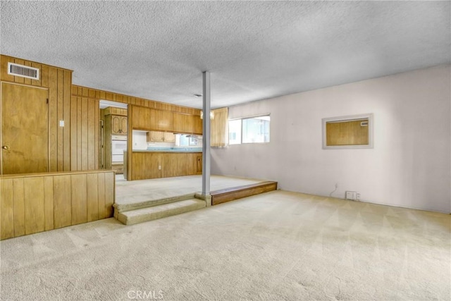 unfurnished living room with carpet floors, a textured ceiling, and wood walls