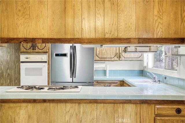 kitchen featuring white appliances, tile counters, and a sink