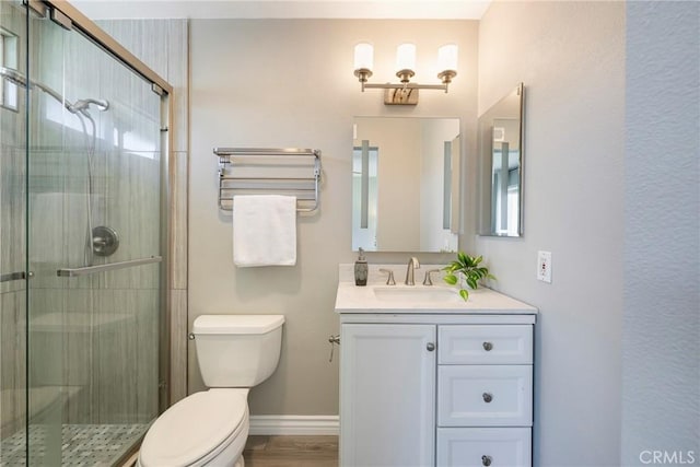 bathroom featuring toilet, a shower stall, vanity, and baseboards