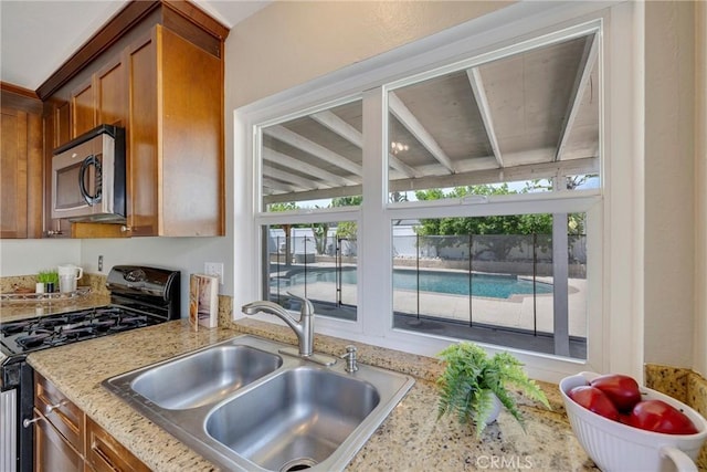 kitchen with gas stove, a sink, stainless steel microwave, brown cabinets, and plenty of natural light