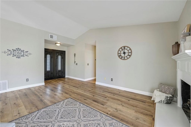 foyer with a fireplace, wood finished floors, vaulted ceiling, and baseboards