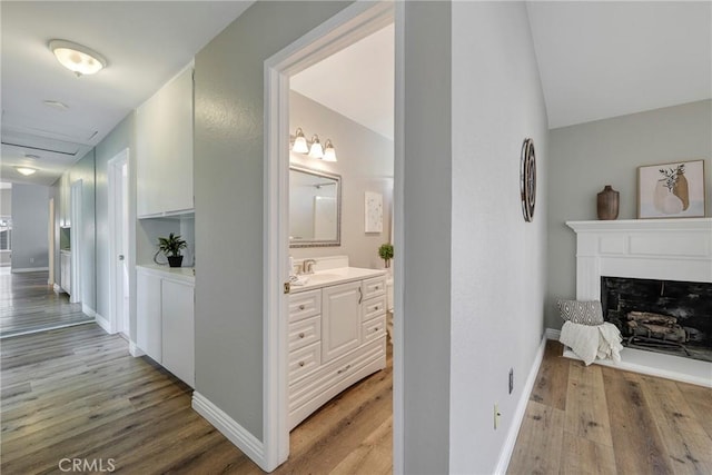 corridor with light wood finished floors, baseboards, a sink, and vaulted ceiling