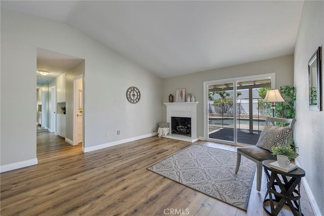 living area with vaulted ceiling, wood finished floors, baseboards, and a fireplace with raised hearth