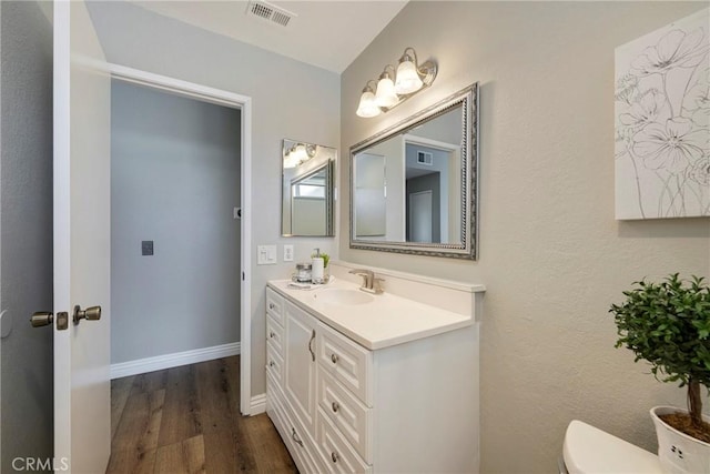 half bathroom featuring toilet, wood finished floors, vanity, and baseboards