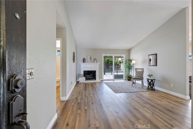 living area featuring vaulted ceiling, wood finished floors, baseboards, and a fireplace with raised hearth