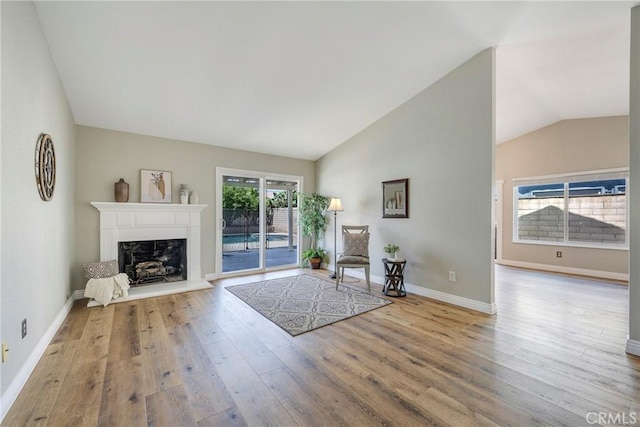 living room with wood finished floors, a fireplace, vaulted ceiling, and baseboards