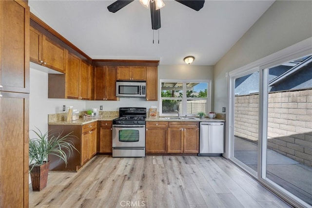 kitchen featuring stainless steel appliances, light wood finished floors, brown cabinets, a ceiling fan, and light stone counters