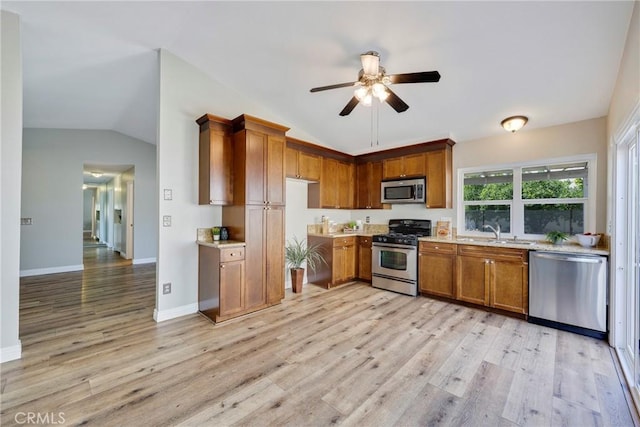 kitchen featuring appliances with stainless steel finishes, lofted ceiling, brown cabinets, a ceiling fan, and a sink